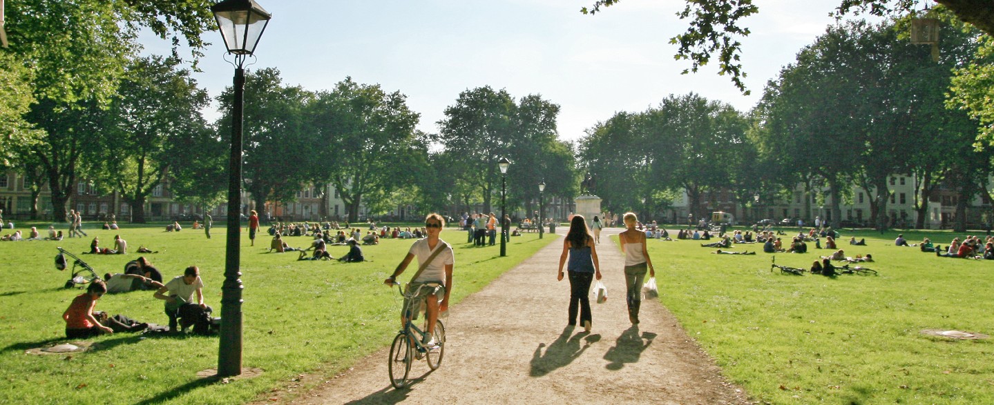 a man riding his bicycle and two girls walking in a green leafy park